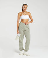 امرأة ترتدي حمالة صدر بيضاء وسروال رياضي ثقيل الوزن باللون الأخضر من Gymshark | United We Sweat مع راحة استثنائية.